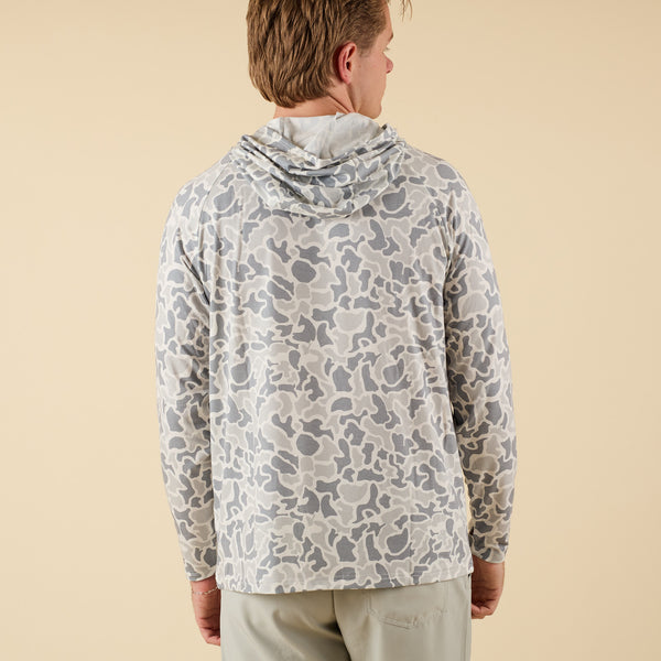 Man wearing a white camo long sleeve hooded t-shirt on a beige background.