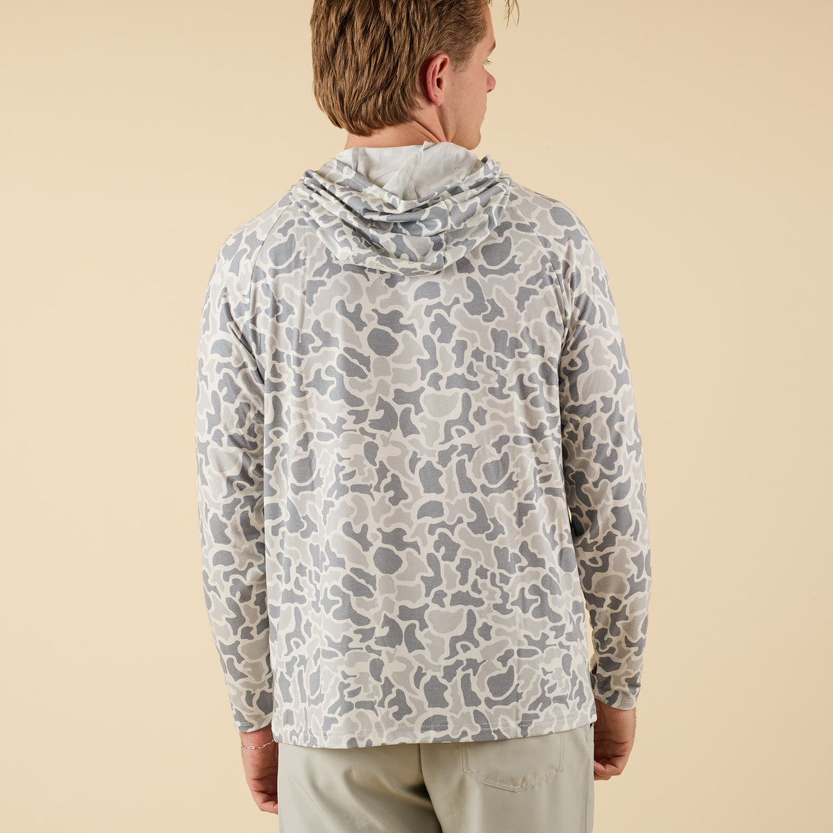 Man wearing a white camo long sleeve hooded t-shirt on a beige background.
