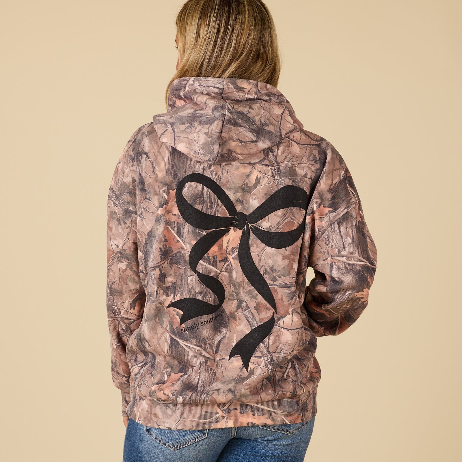 Camouflage jacket with a black bow design on the back, worn by a person.