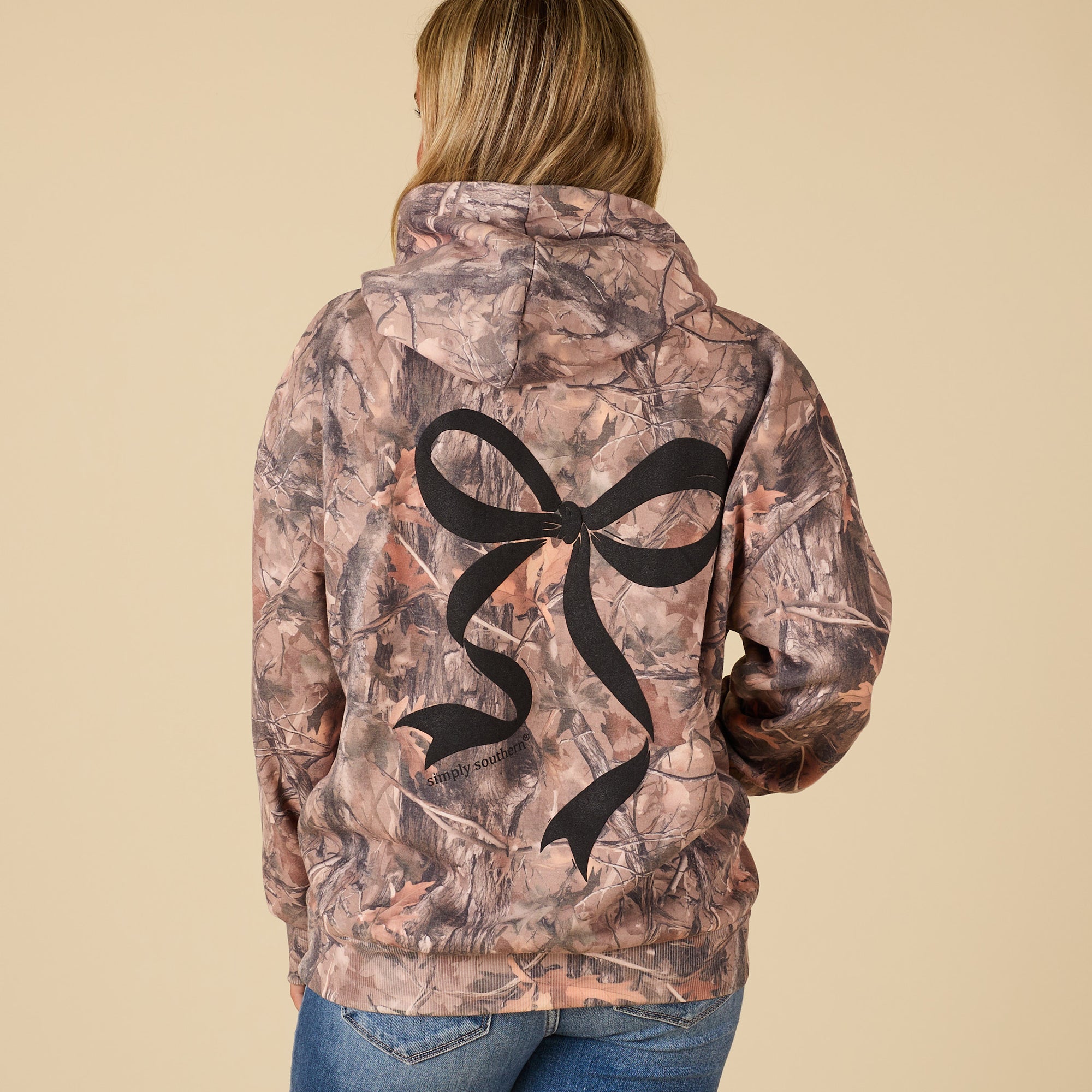 Camouflage jacket with a black bow design on the back, worn by a person.