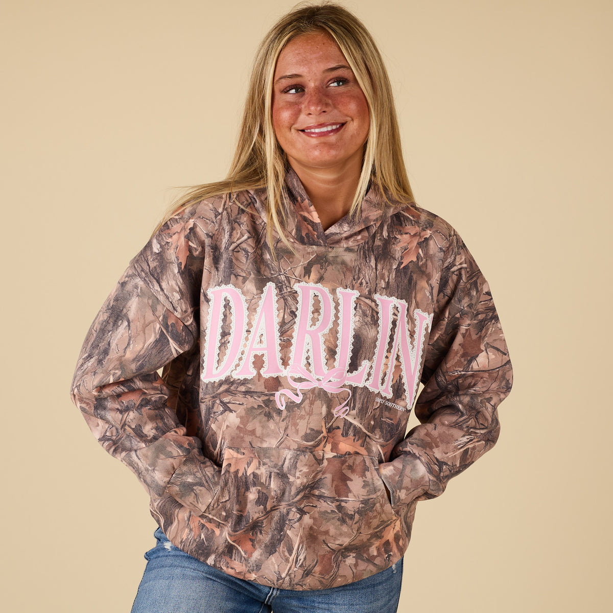 Person wearing a camouflage hoodie with 'Darlin' text on a beige background