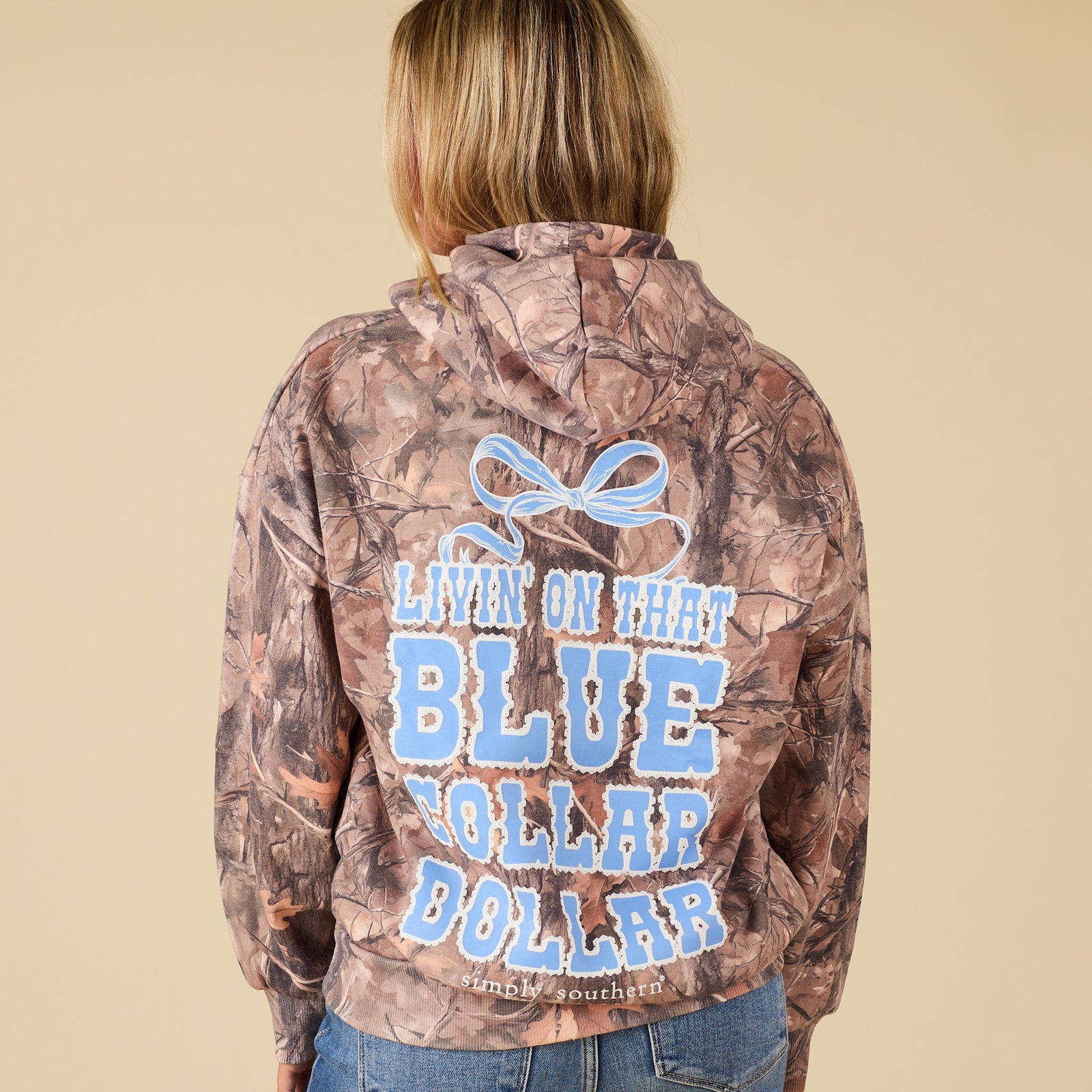 Camouflage jacket with text and logo on the back, worn by a person against a beige background