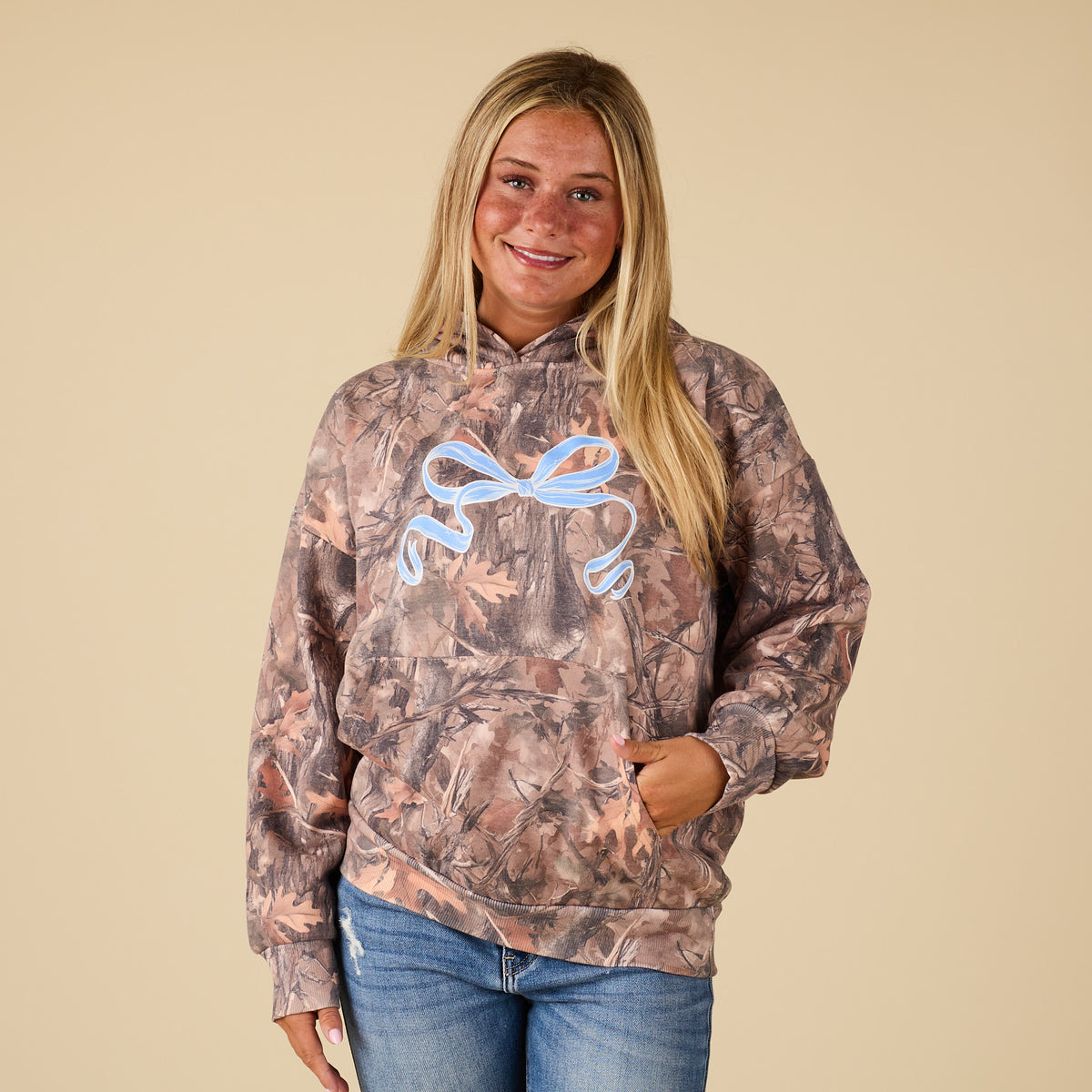 Person wearing a camouflage hoodie with a logo on a beige background