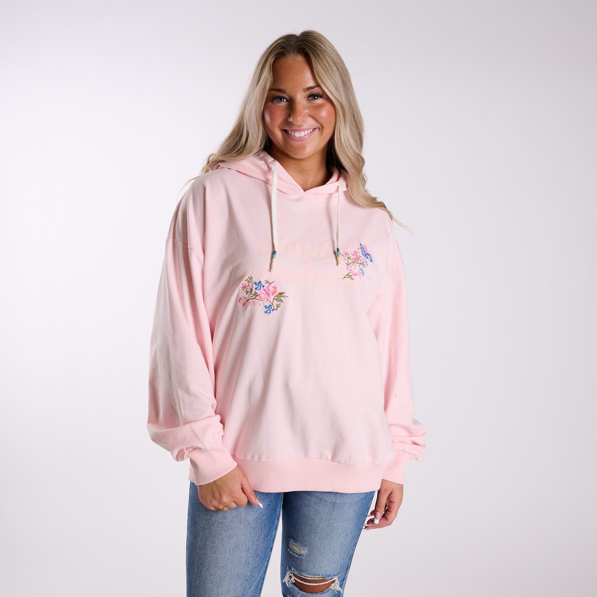 Woman wearing a pink hoodie with floral designs on a white background