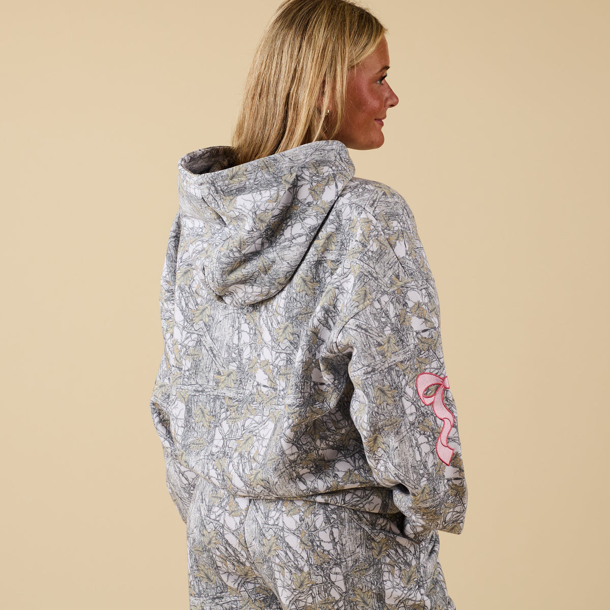 Back view of Alice Camo Hoodie with camo print and pink bow accent on sleeve.