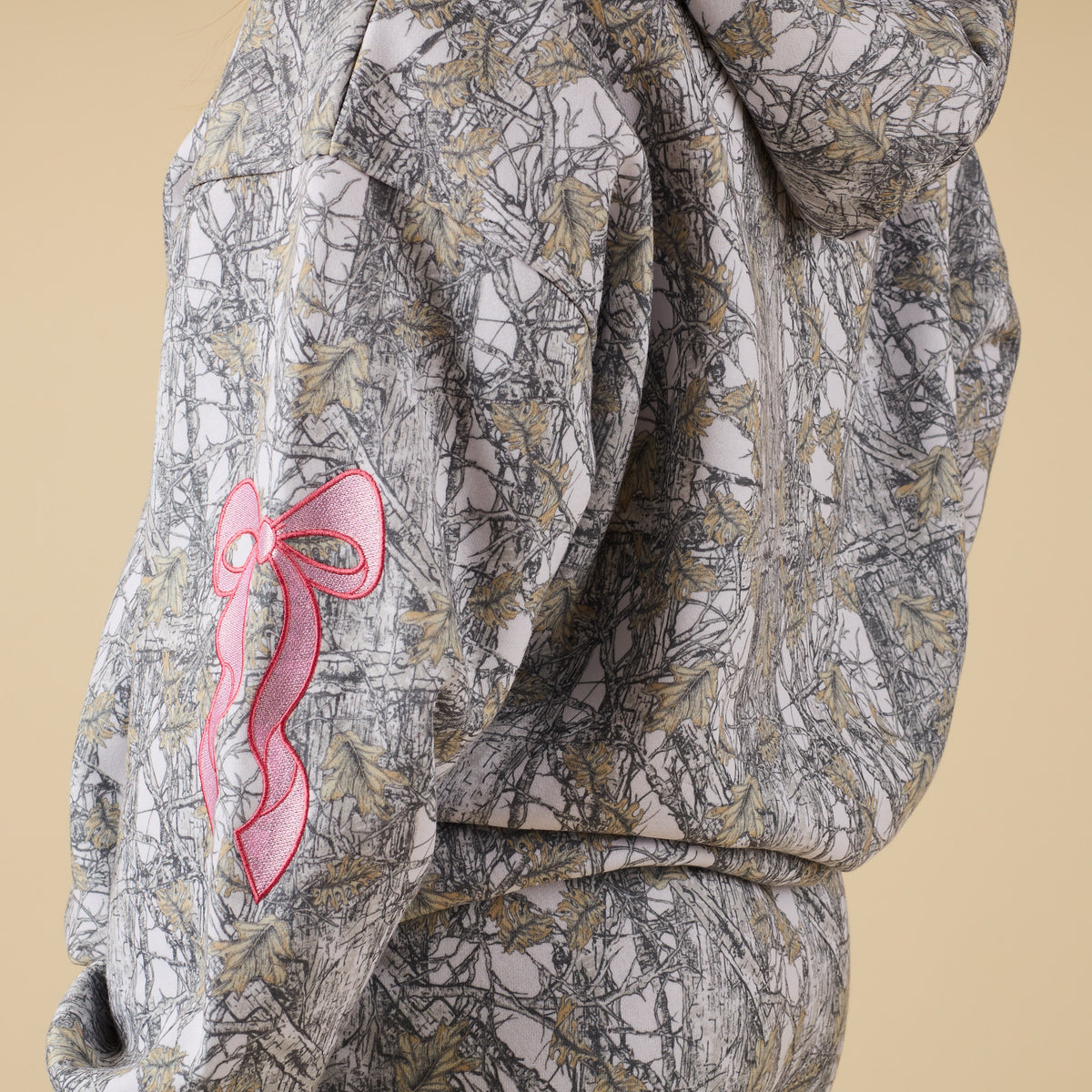 Close-up of Alice Camo Hoodie sleeve showing pink embroidered bow detail.