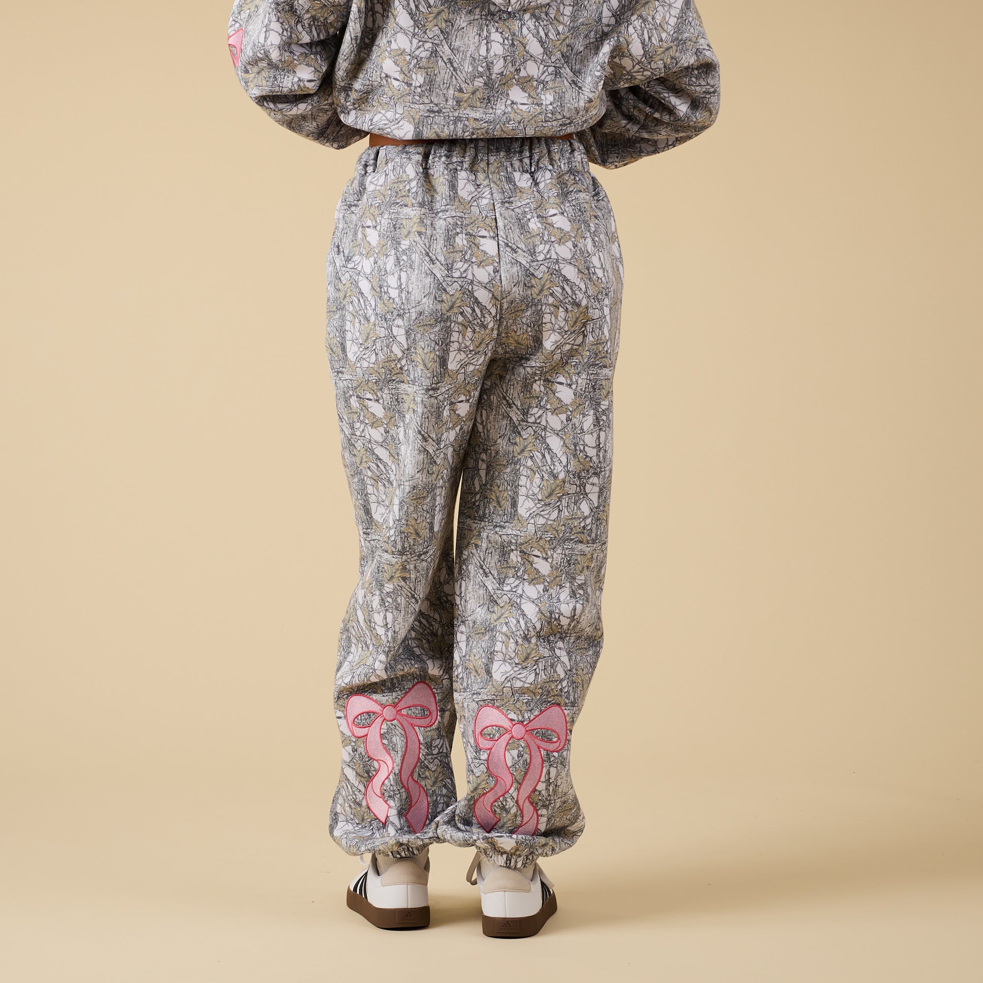 Full back view of camo sweatpants with large pink bow embroidery on calves.