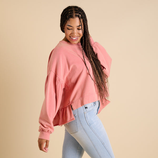  Woman wearing a pink sweatshirt and light blue jeans against a beige background