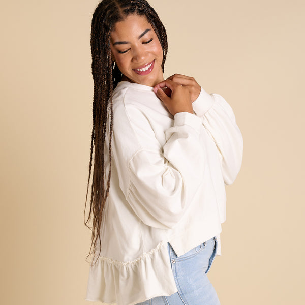  Woman wearing a white blouse with ruffled sleeves against a beige background