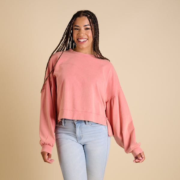 Woman wearing a pink sweatshirt and light blue jeans against a beige background