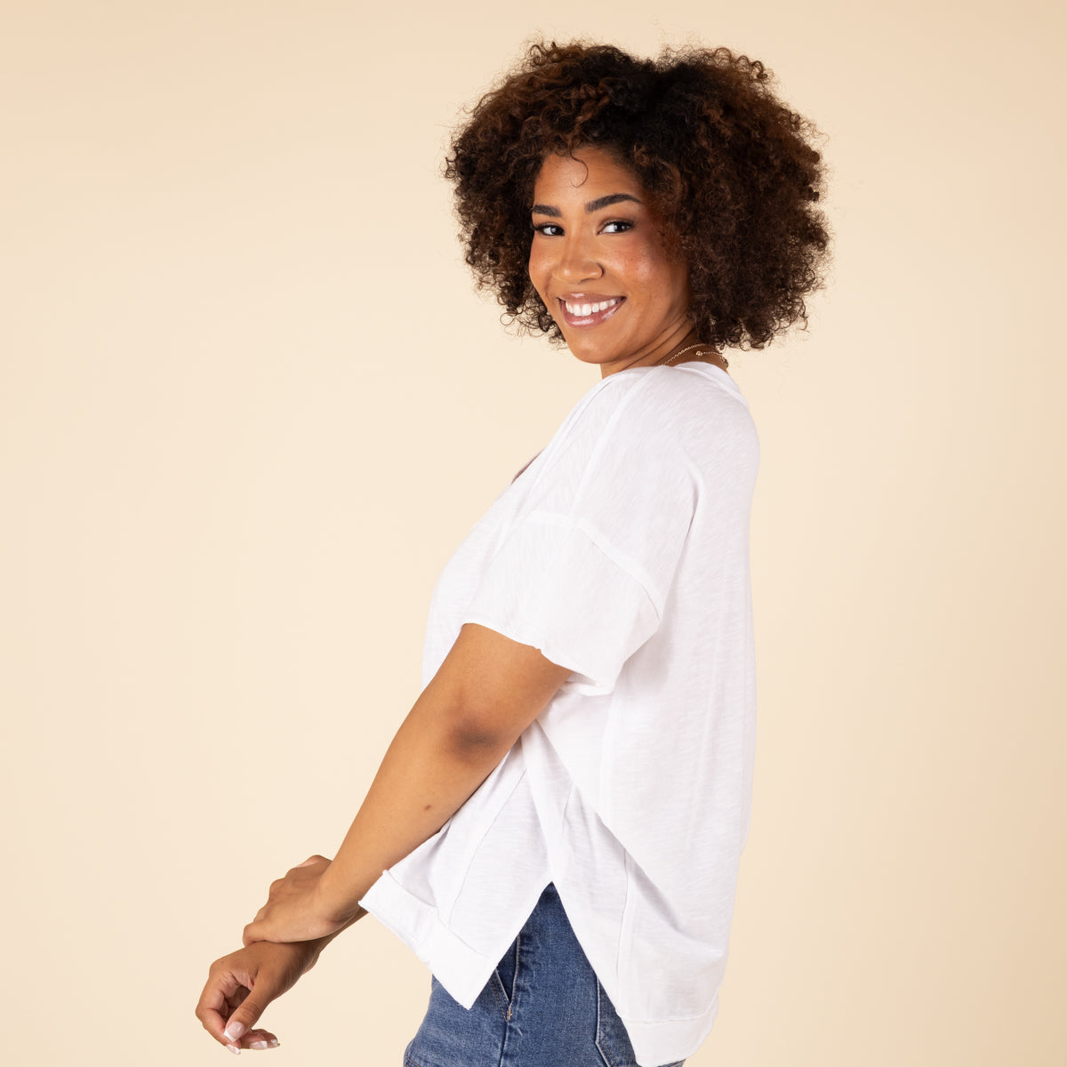 Woman wearing a white t-shirt and blue jeans against a beige background
