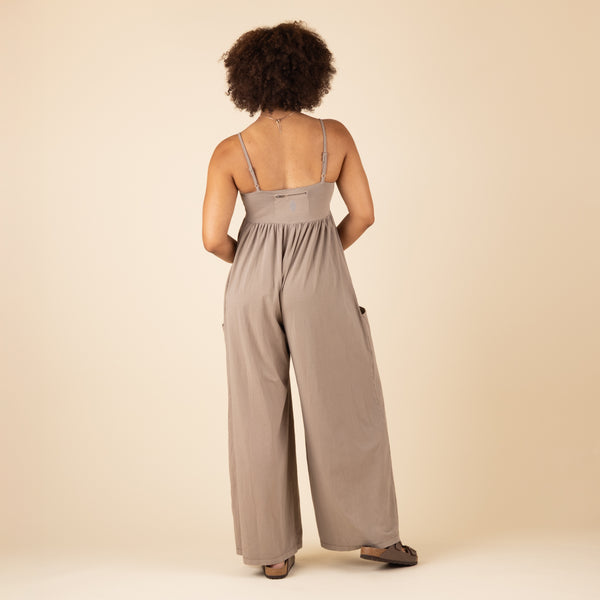  Back view of the taupe spaghetti strap jumpsuit with a smocked back detail and wide-leg silhouette, styled with sandals.