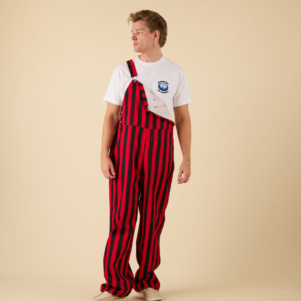 Front view of a man wearing red and black striped overalls with one shoulder strap unbuttoned.