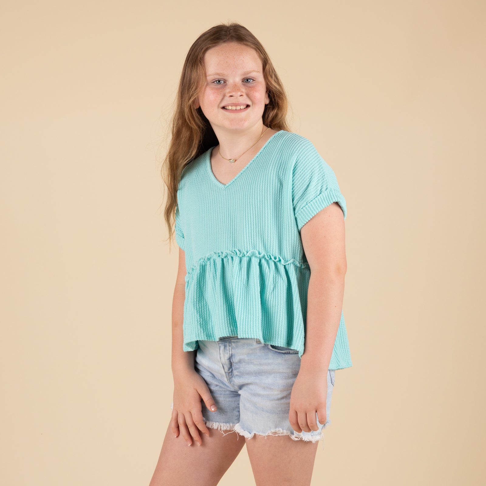 Charlotte Avery Youth Ribbed Short Sleeve Babydoll Top in mint, front angle showing v-neckline and ruffled waist. Paired with light denim shorts.