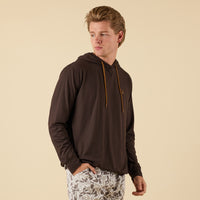 Men’s brown performance hooded long sleeve shirt with contrast drawstrings and small chest logo, styled with light camo shorts against a neutral studio background.