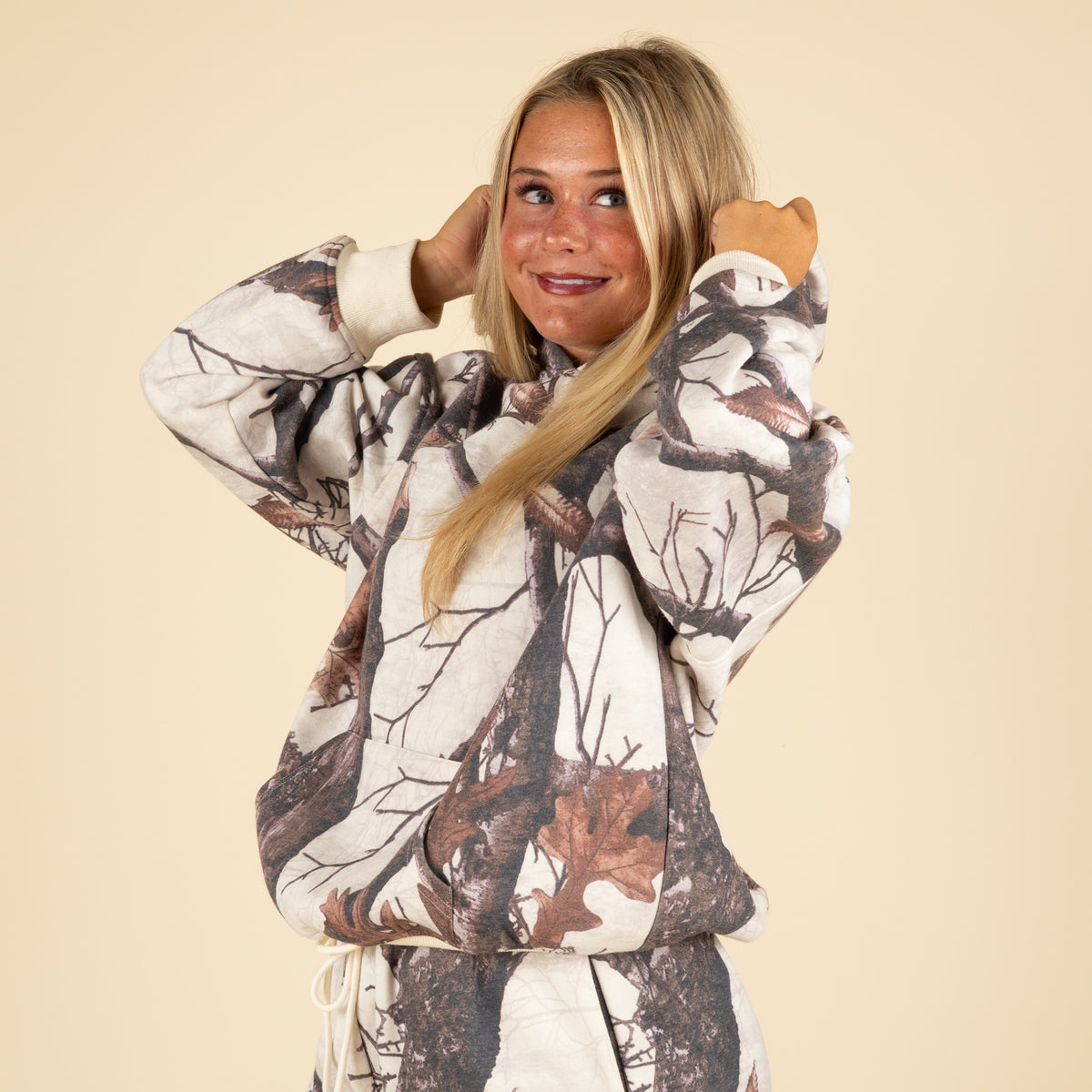 Woodland camo hoodie by Pretty Garbage shown on model adjusting hood.