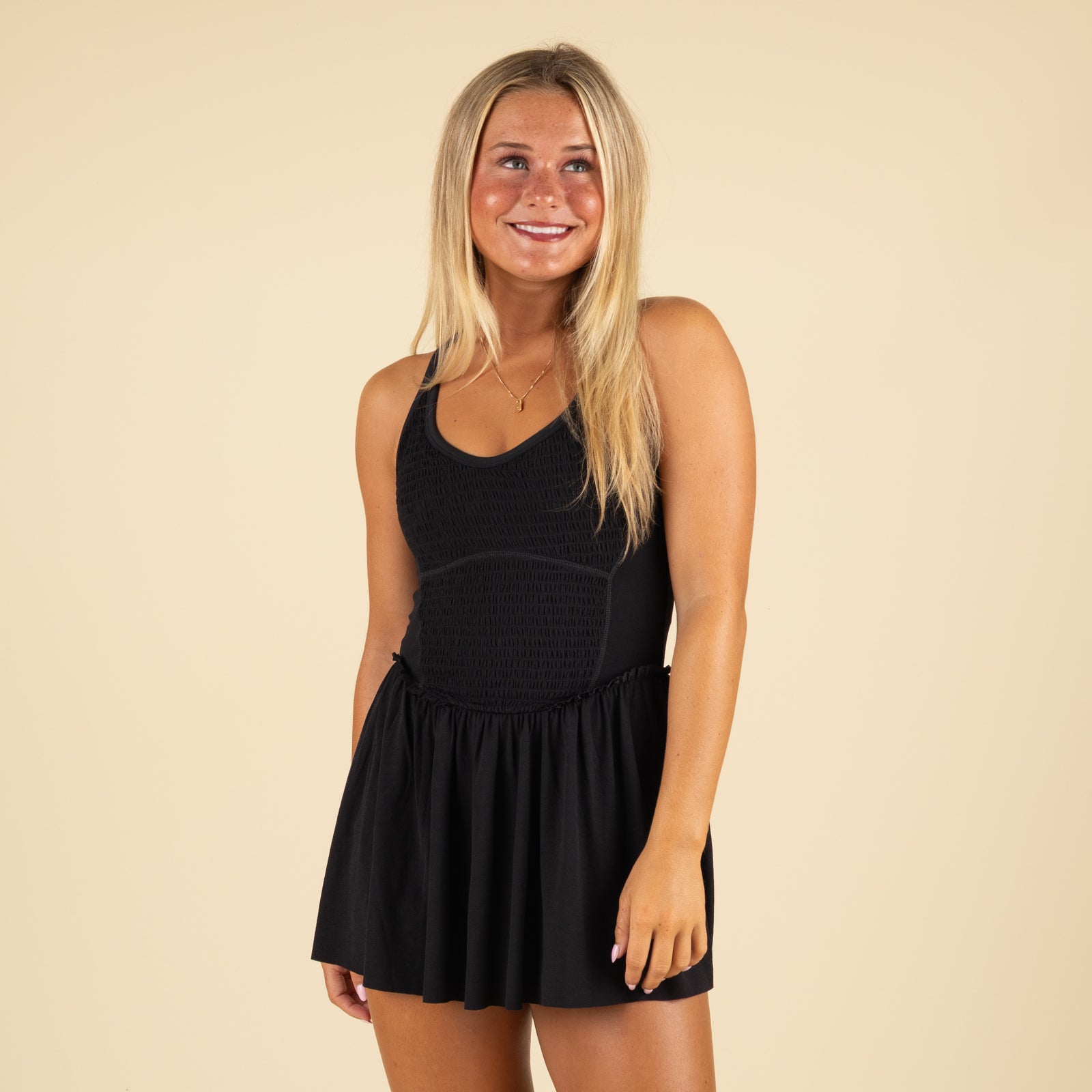 Front-facing view of model wearing black athletic dress, smiling with one hand by her side.