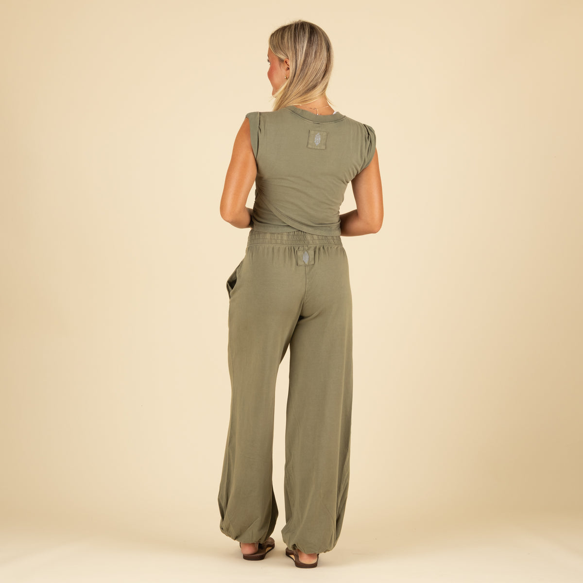 Full back view of woman in olive green jogger set with ruched twist-front top and relaxed wide-leg pants with elastic cuffs and side pockets.