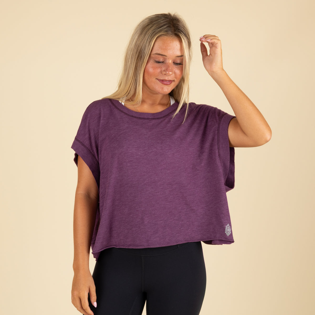 Front view of a woman wearing a loose-fit purple cropped top with short sleeves, paired with black leggings.