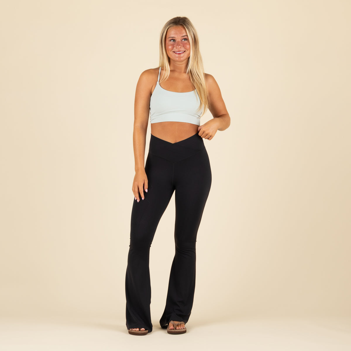 Local Girl black flare leggings with crossover waistband, shown from the front on model paired with light blue sports bra.