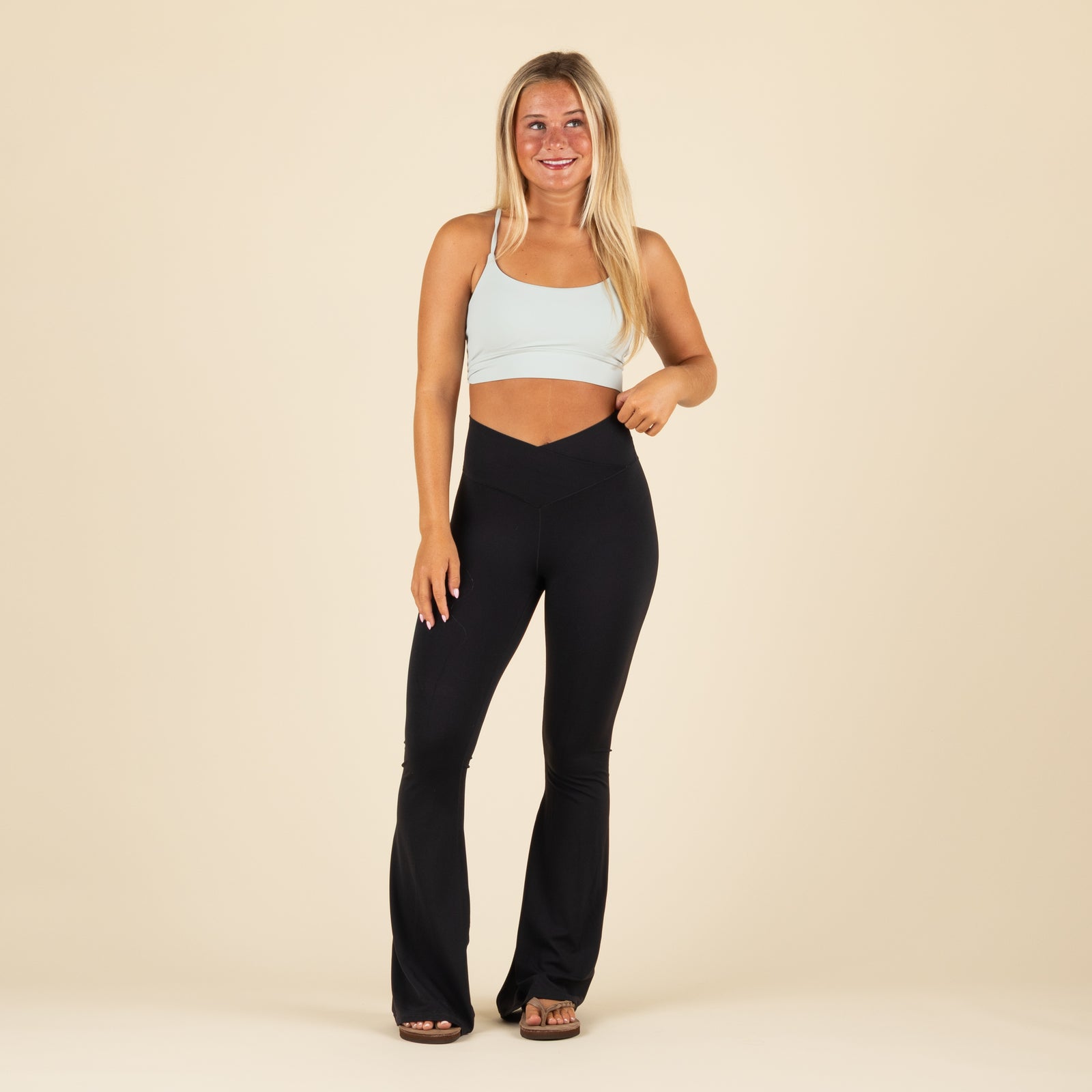 Local Girl black flare leggings with crossover waistband, shown from the front on model paired with light blue sports bra.
