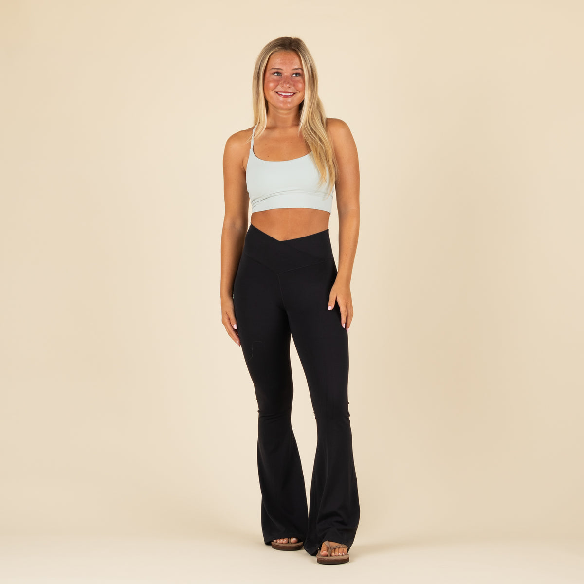 Local Girl black flare leggings with crossover waistband, shown from the front on model paired with light blue sports bra.