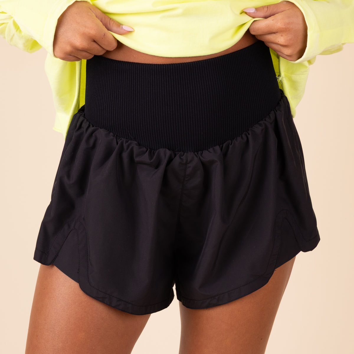 Person wearing black shorts and a yellow top on a beige background
