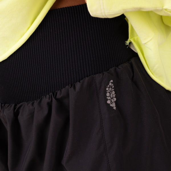 Close-up of a black skirt with a floral embroidery detail, worn over a yellow garment.