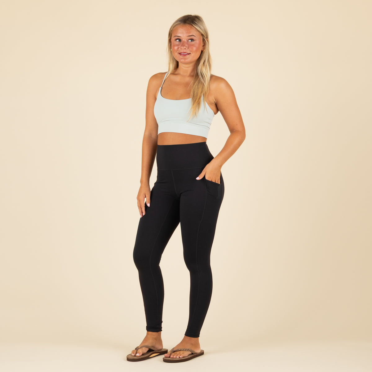 Woman wearing a light blue sports bra and black leggings on a beige background