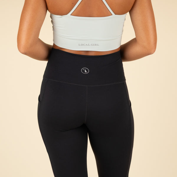 Person wearing a light green sports bra and black leggings with a beige background