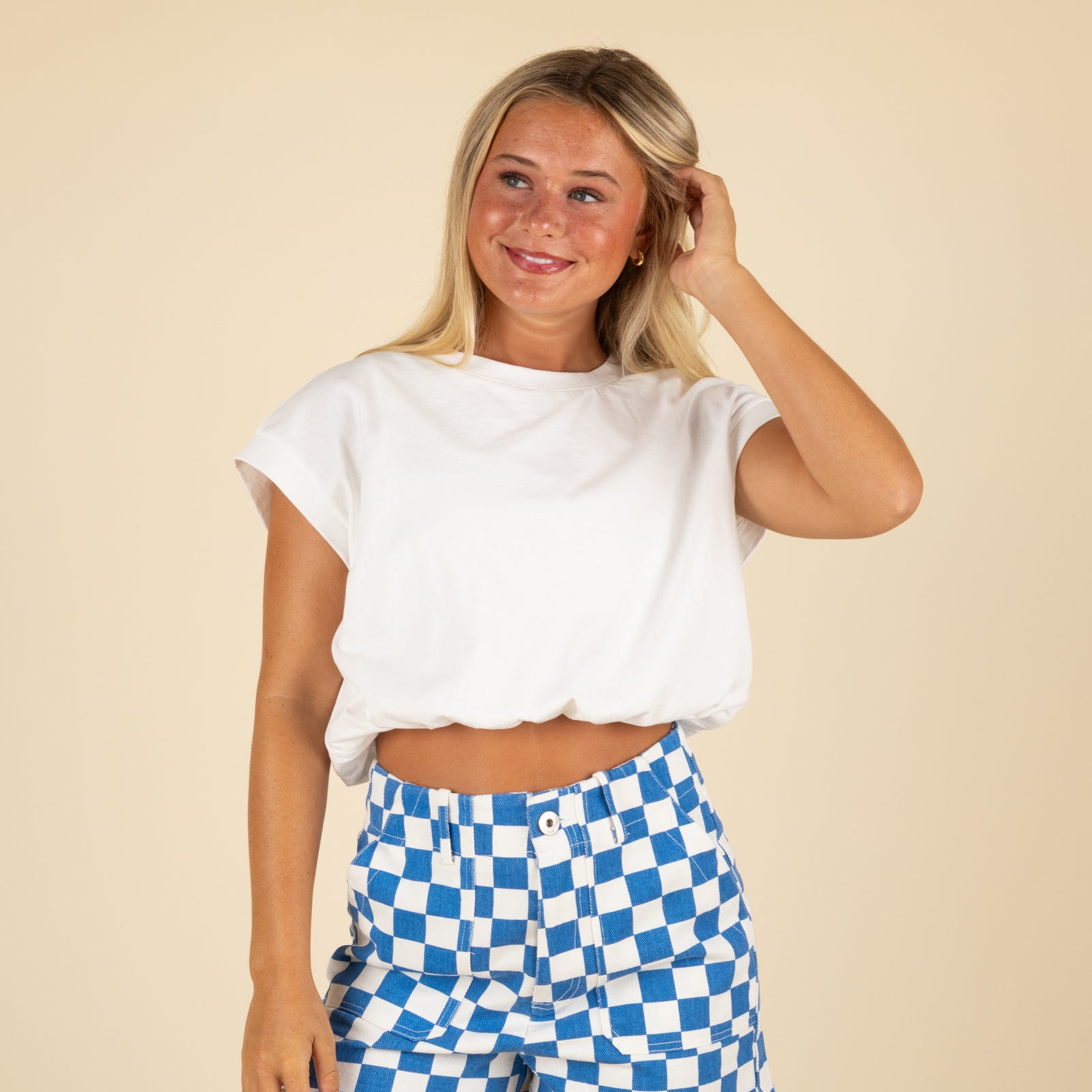 Woman wearing a white top and blue checkered pants on a beige background