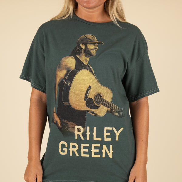 Close-up of Riley Green t-shirt front graphic with Riley holding a guitar and bold “Riley Green” text.