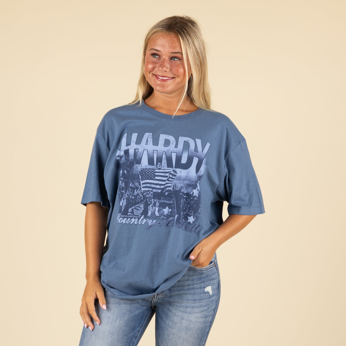 Woman wearing a blue oversized Hardy “Country As Hell” graphic t-shirt with concert crowd and American flag design.