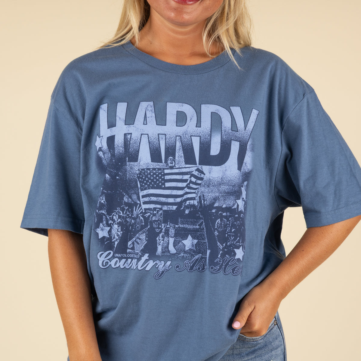 Close-up of blue Hardy “Country As Hell” graphic t-shirt showing distressed-style concert crowd and American flag design.
