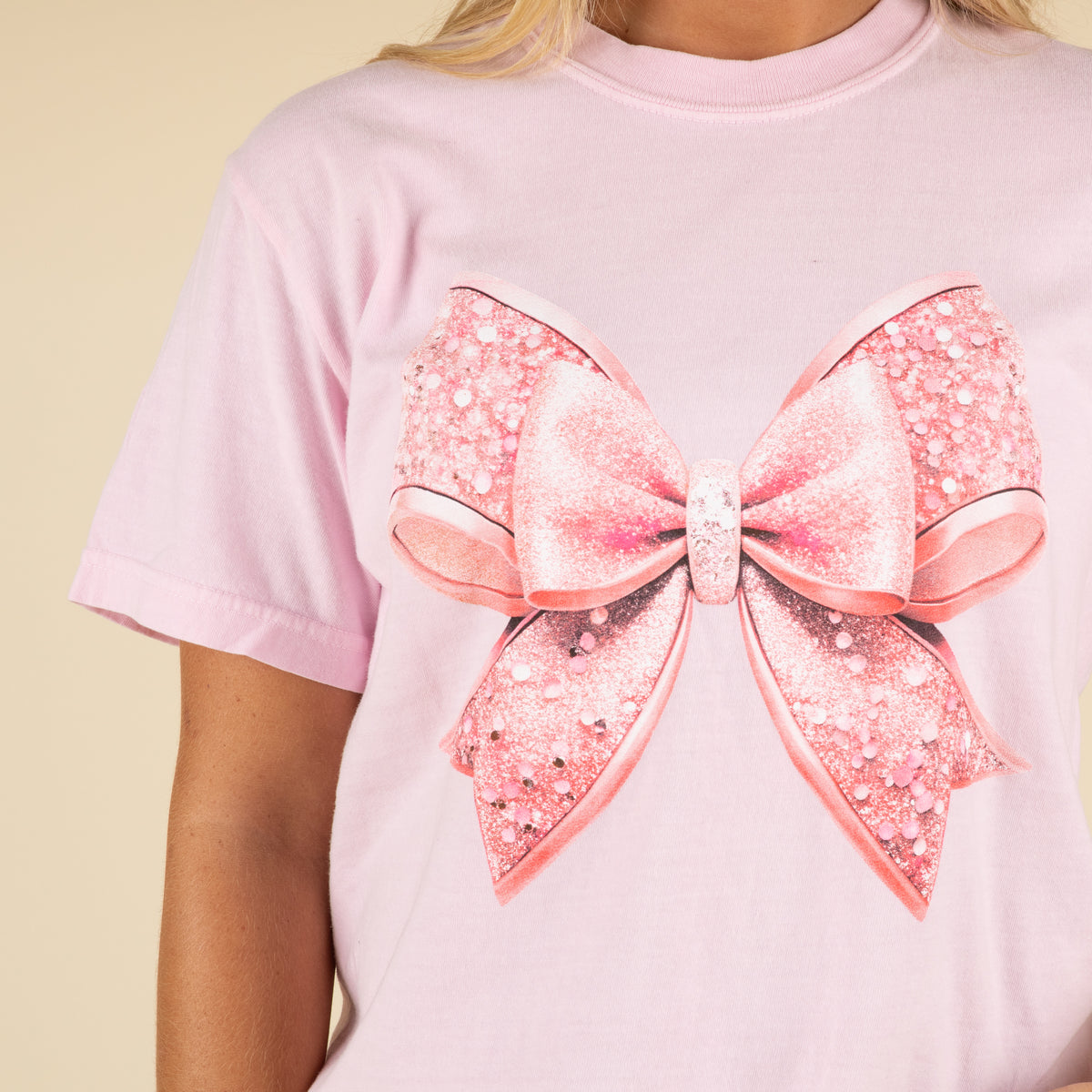 Pink t-shirt with a large glittery bow design on a beige background