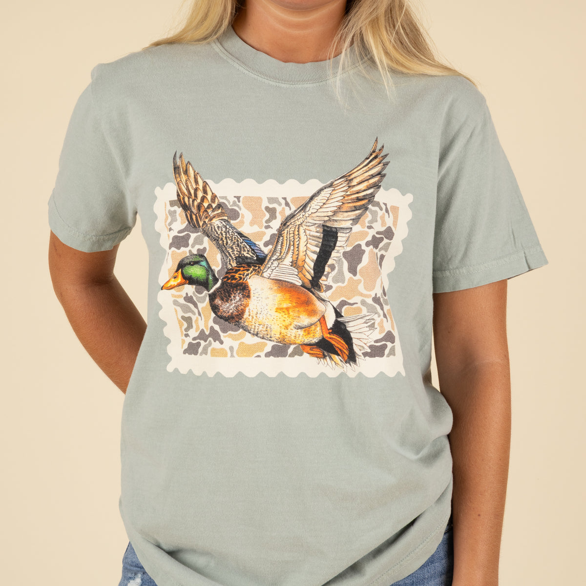Person wearing a light green t-shirt with a duck graphic on a beige background