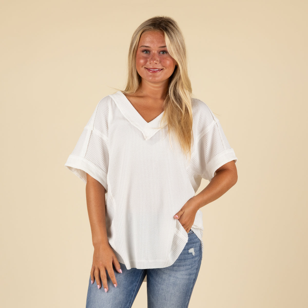front view of a woman wearing an oversized white ribbed vneck top paired with medium denim jeans.