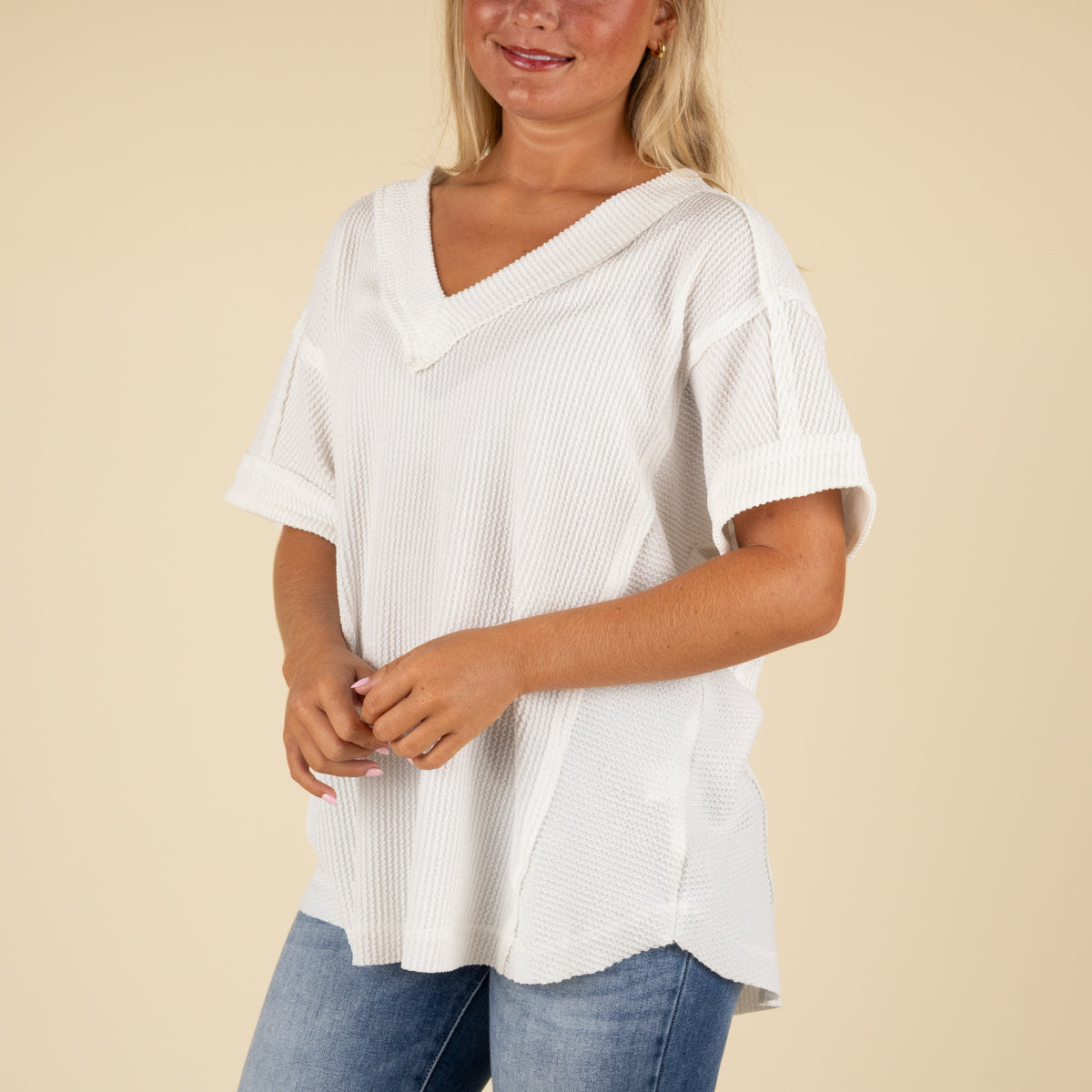 closeup front angled view of a woman wearing an oversized white ribbed vneck top paired with medium denim jeans.