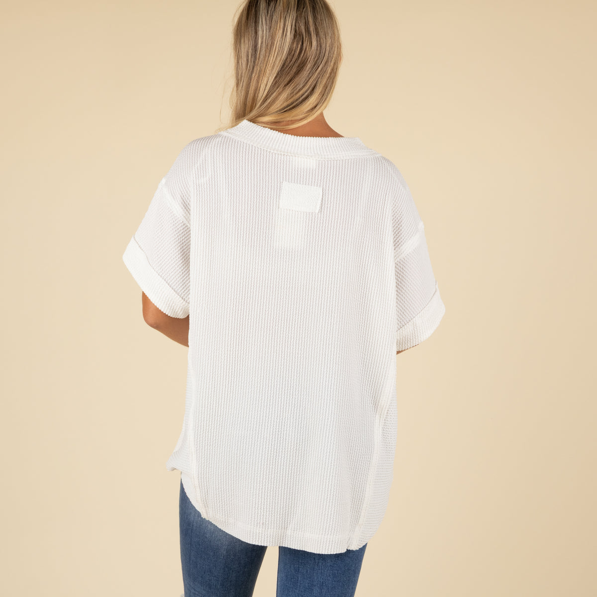 back view of a woman wearing an oversized white ribbed vneck top paired with medium denim jeans.
