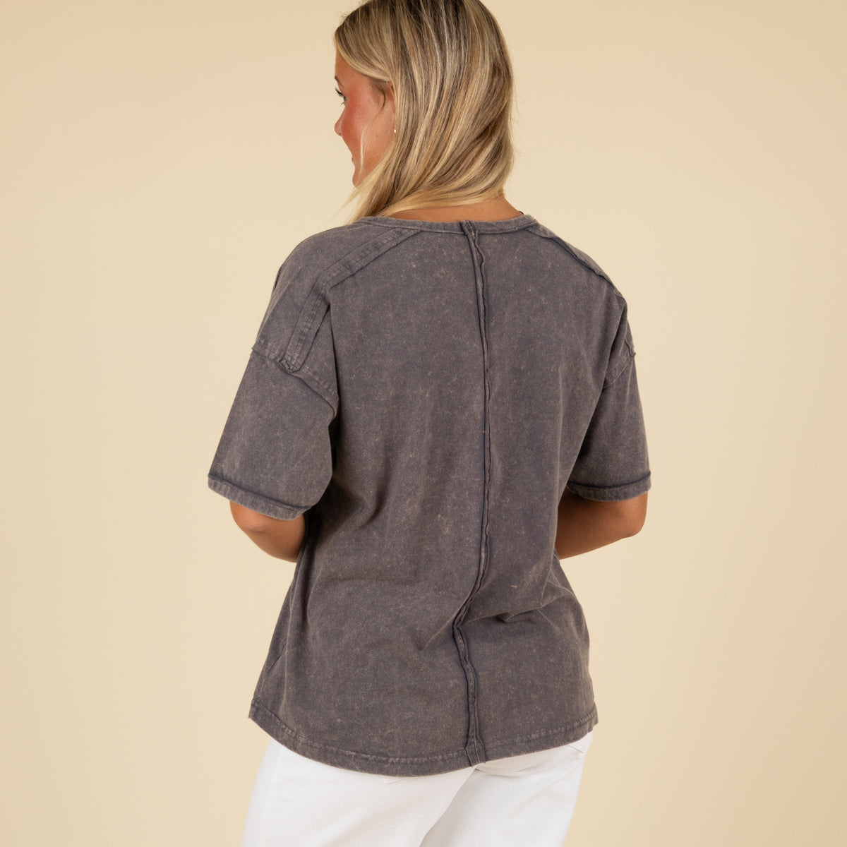 Back view of a woman wearing a charcoal gray pocket t-shirt with an exposed center seam down the back.