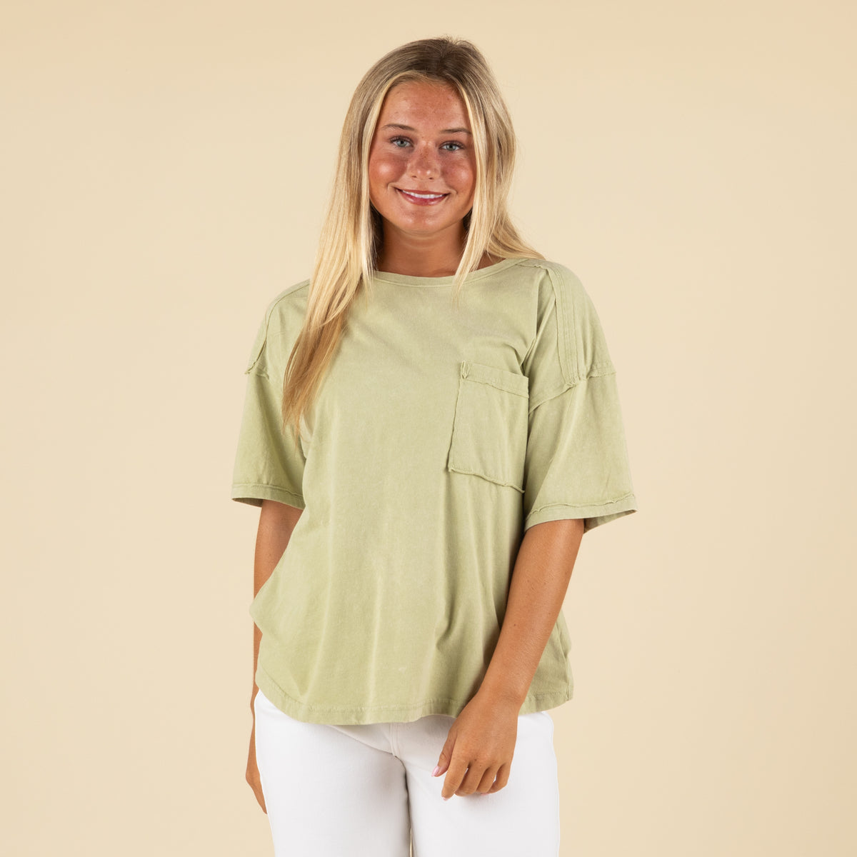 Front view of a woman in a light sage green oversized t-shirt featuring a front pocket and relaxed fit.