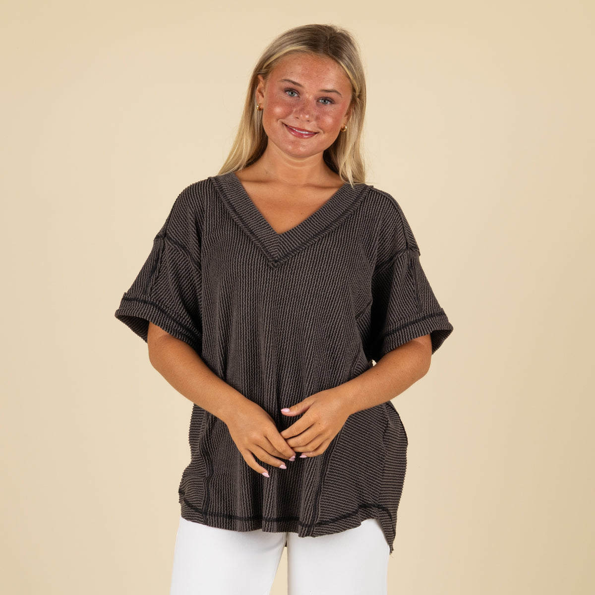 front angled view of a woman wearing an oversized charcoal ribbed vneck top paired with white denim jeans.