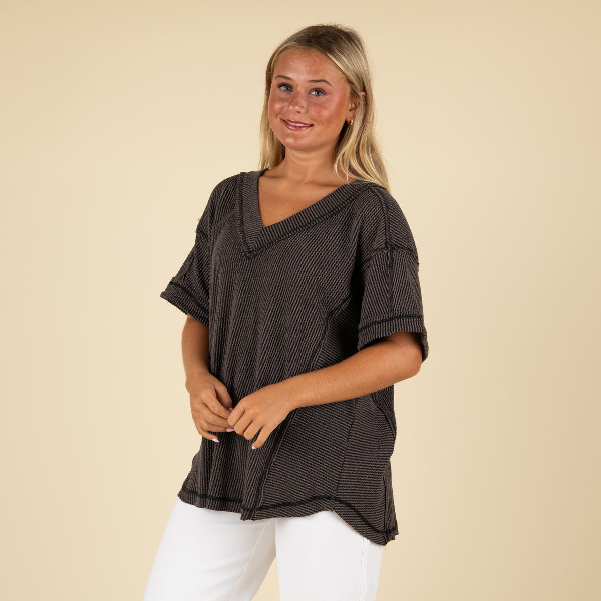 front angled view of a woman wearing an oversized charcoal ribbed vneck top paired with white denim jeans.