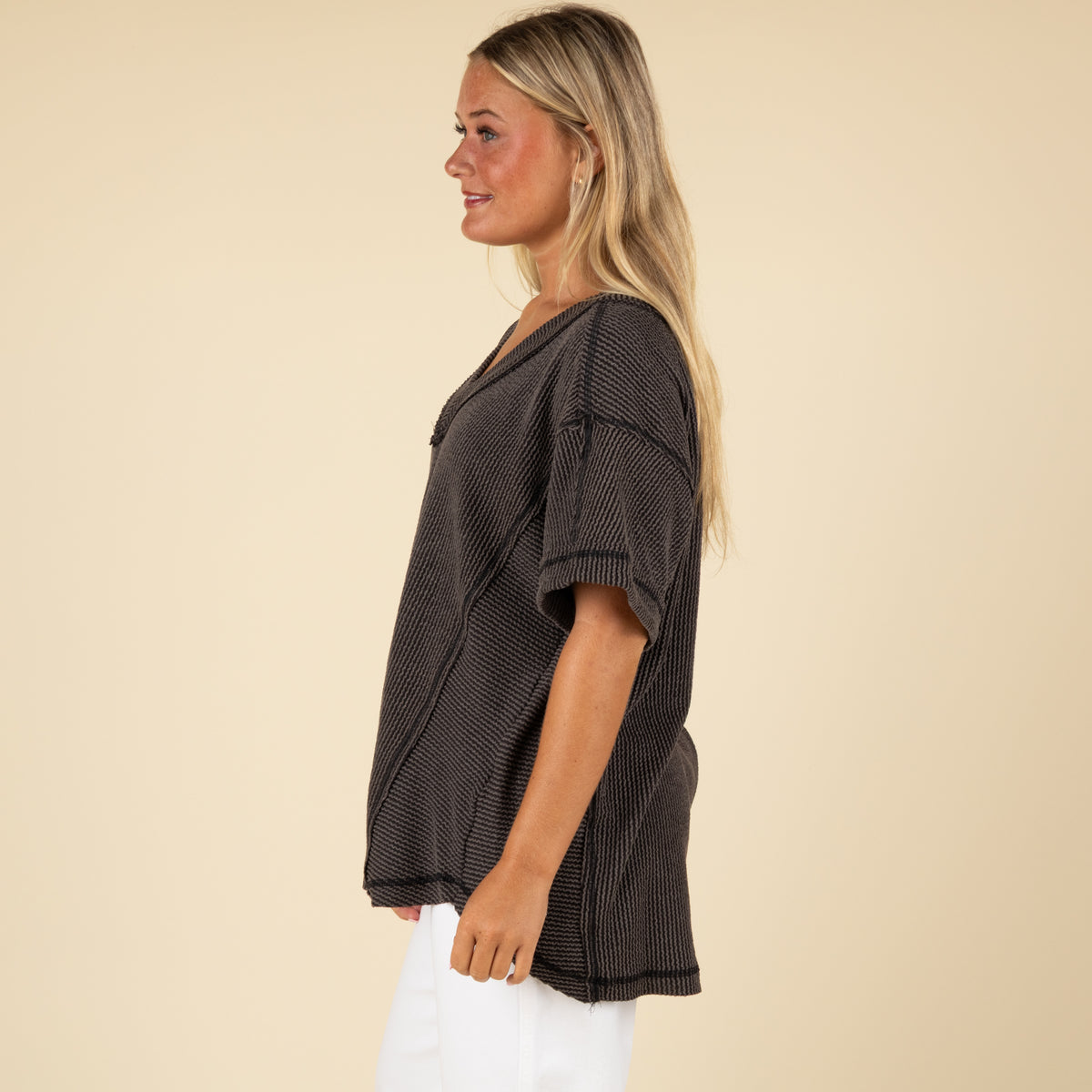 side view of a woman wearing an oversized charcoal ribbed vneck top paired with white denim jeans.