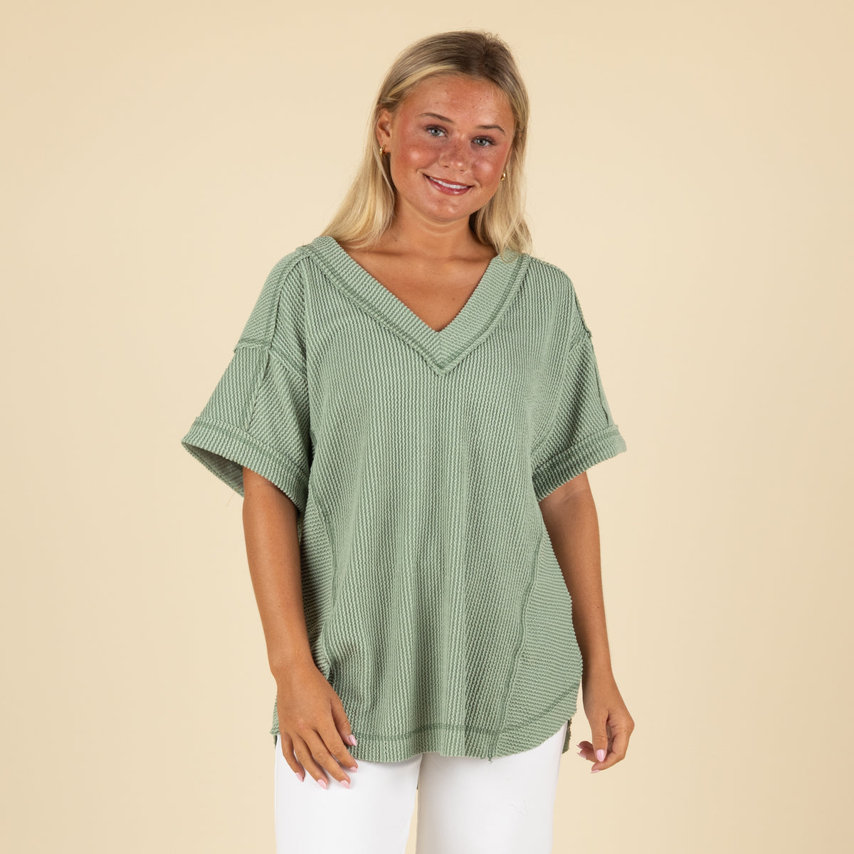 front angled view of a woman wearing an oversized sage ribbed vneck top paired with white denim jeans.