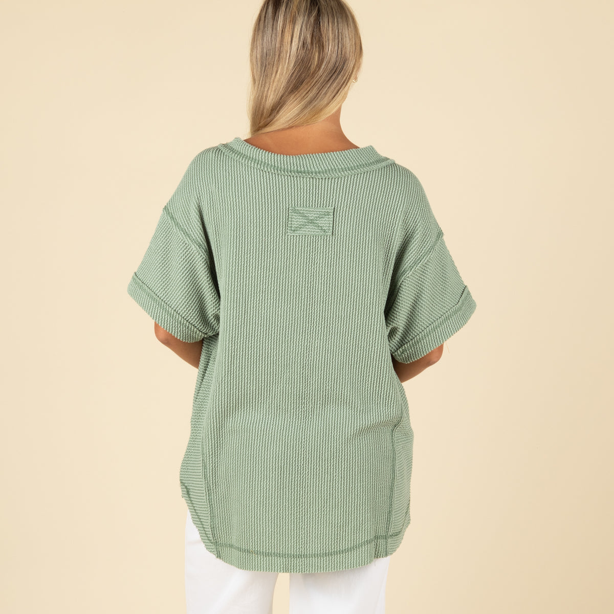back view of a woman wearing an oversized sage ribbed vneck top paired with white denim jeans.