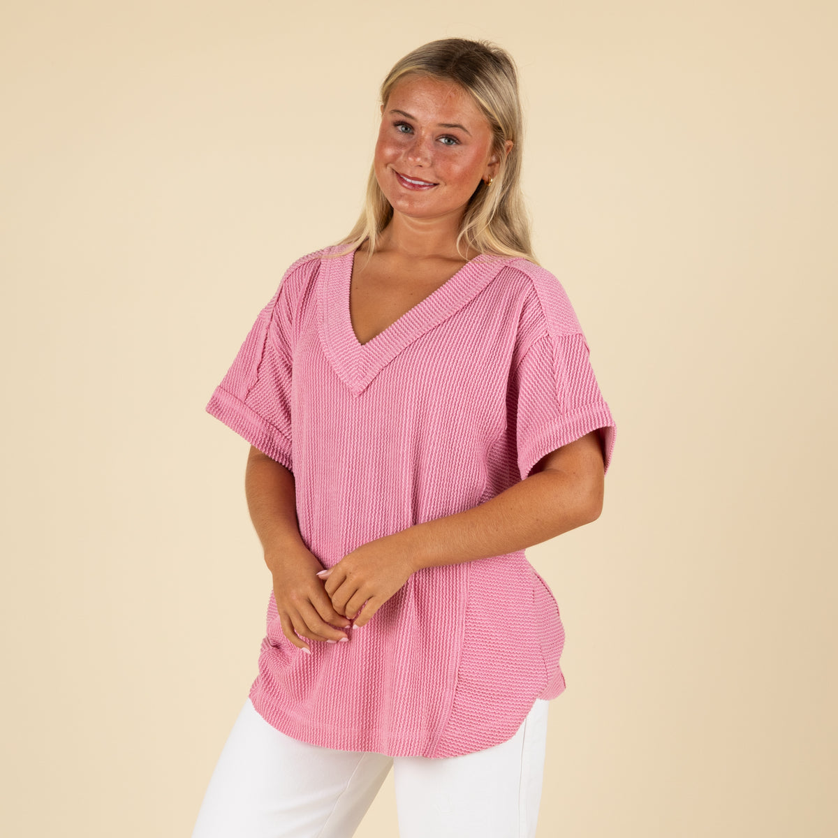 front angled view of a woman wearing an oversized pink ribbed vneck top paired with white denim jeans.