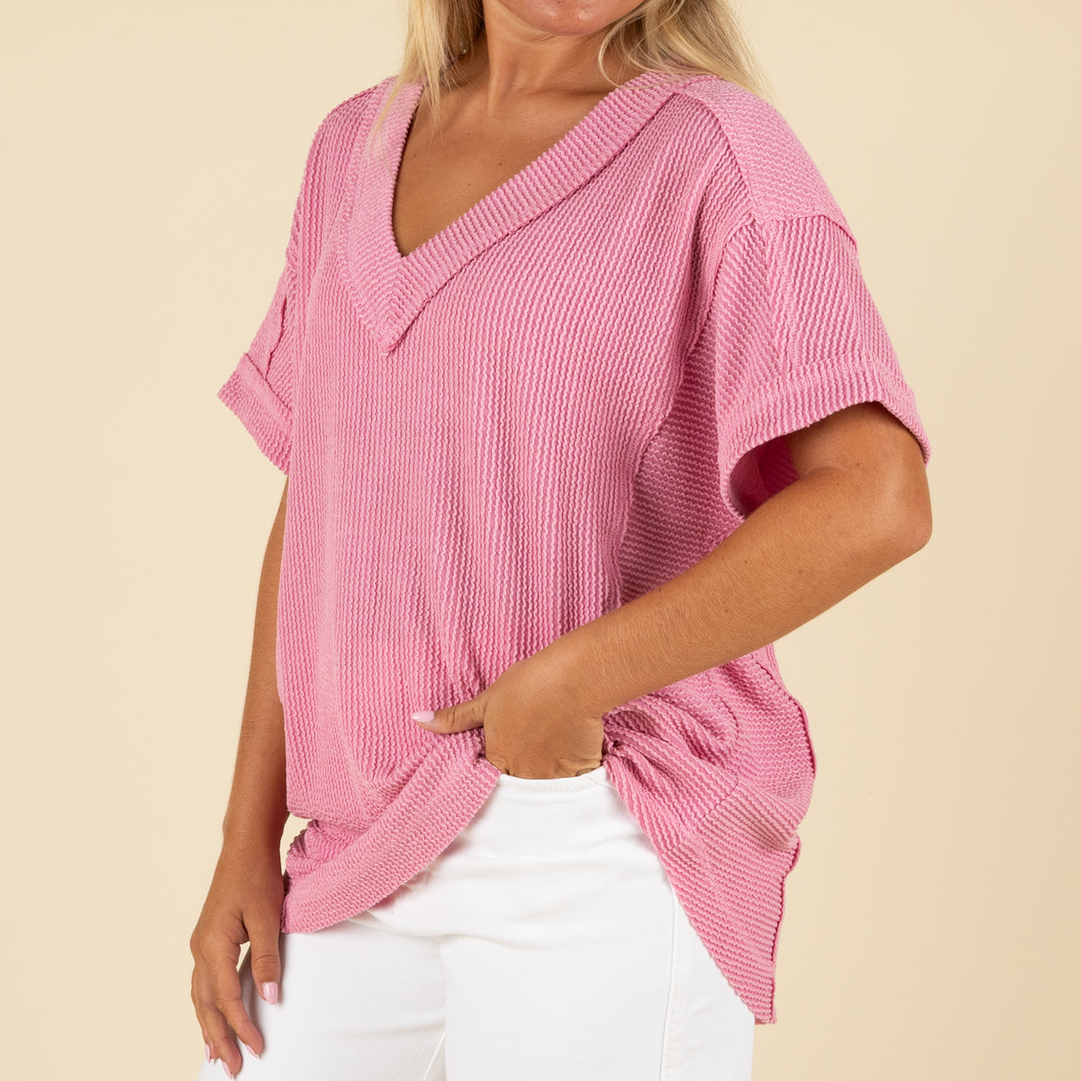 close up front angled view of a woman wearing an oversized pink ribbed vneck top paired with white denim jeans.