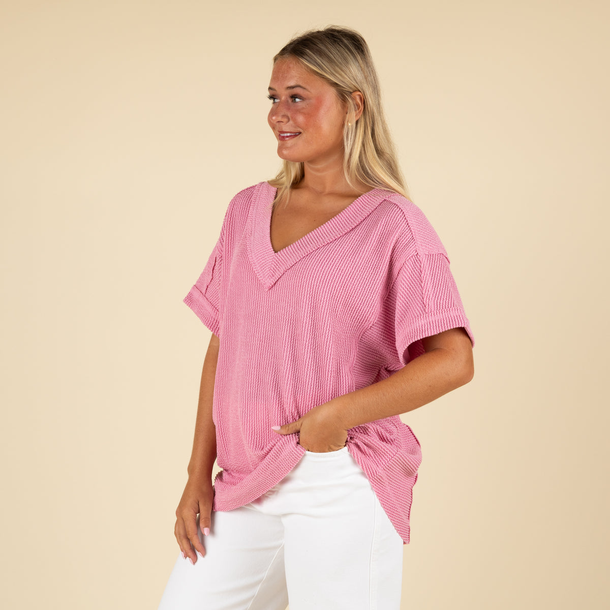 side angled view of a woman wearing an oversized pink ribbed vneck top paired with white denim jeans.