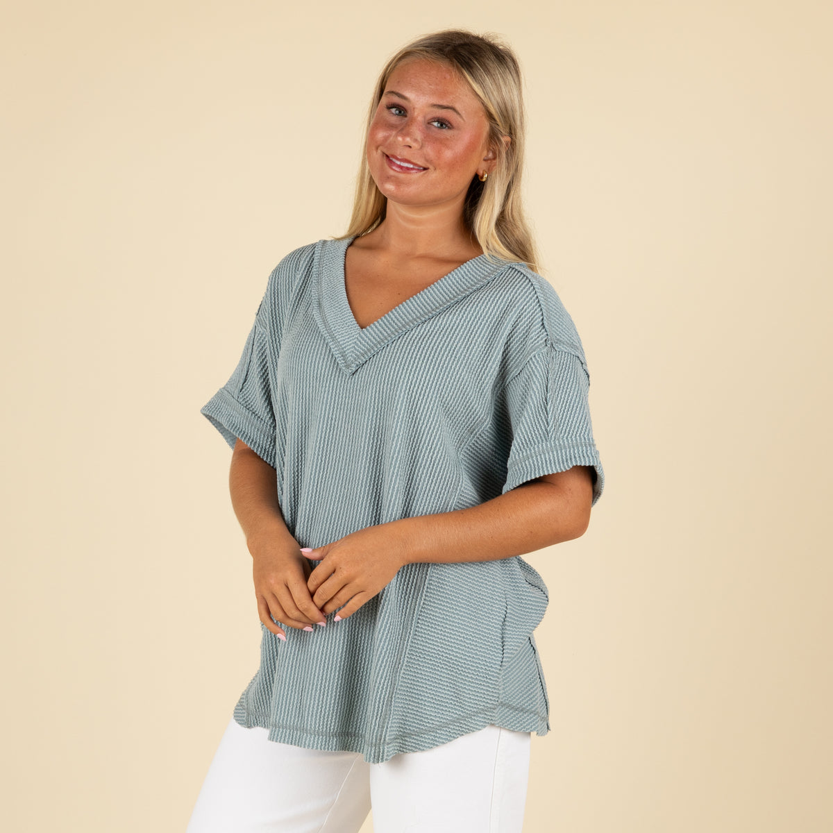 front angled view of a woman wearing an oversized slate blue ribbed vneck top paired with white denim jeans.